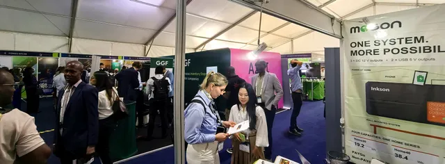 A busy exhibition tent at the Global Off-Grid Solar Forum & Expo 2026, with a visitor reading a MOSON leaflet at booth 32