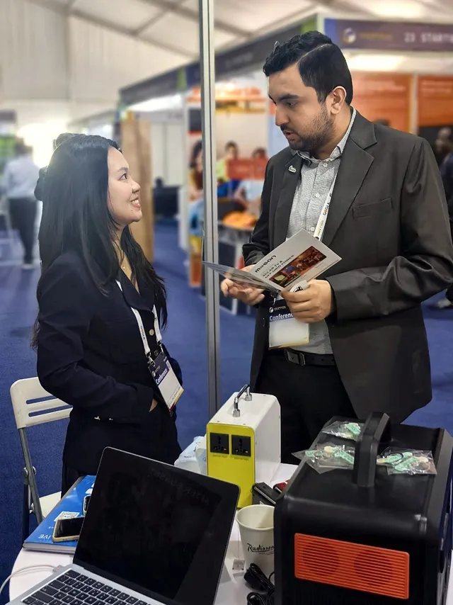 A visitor reading the MOSON brochure at booth 32, with solar home system and portable power station samples on the table