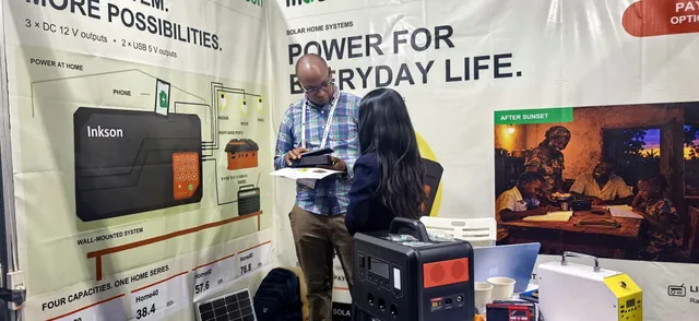 A visitor holding the H Series solar home system and reading a leaflet at booth 32